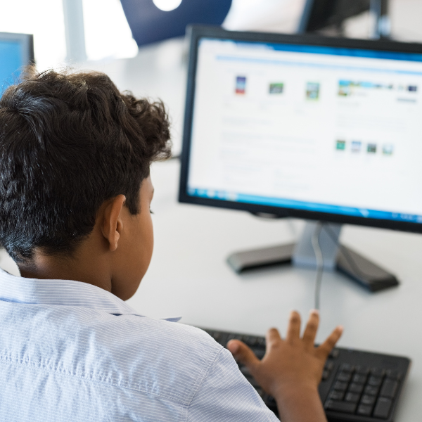 A young boy sits at a computer screen typing on a keyboard