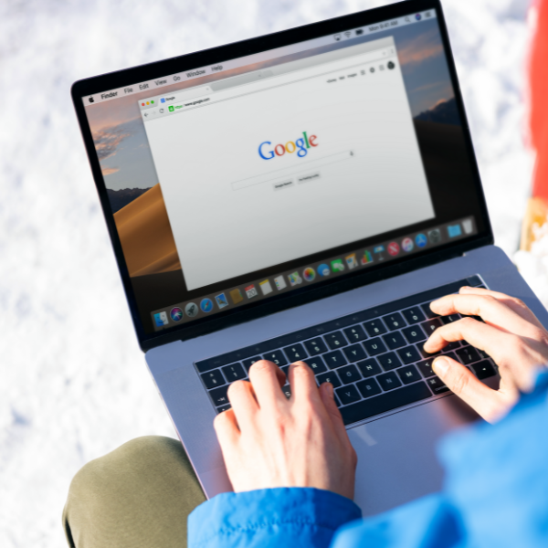 A person wearing a blue jacket is typing on a laptop keyboard with a Google search engine displayed