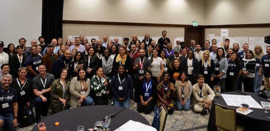 The School Teams AI Collaborative at the convening in Denver, Colorado. It is a large group photo taken in a conference room. Approximately 70-80 diverse professionals are gathered together, arranged in multiple rows, with some people standing and others kneeling in the front.